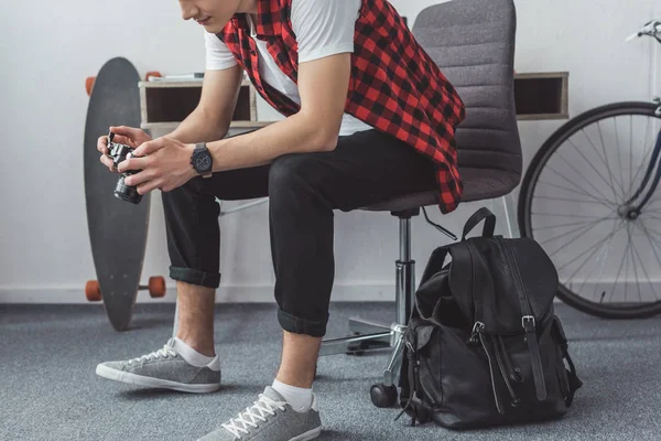 Cropped view of young man with film camera sitting on chair with backpack — Stock Photo