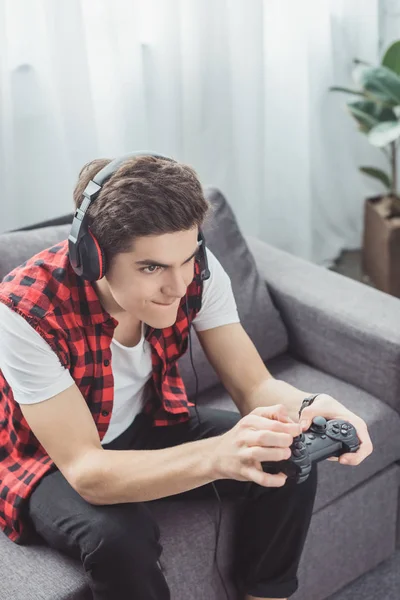 Adolescent garçon avec casque jouer jeu vidéo avec joystick à la maison — Photo de stock