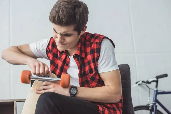 Young skater repairing his longboard at home — Stock Photo