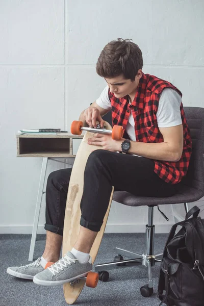 Handsome teen skater fixing his longboard at home — Stock Photo