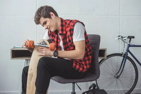 Teen skateboarder fixing his longboard at home — Stock Photo