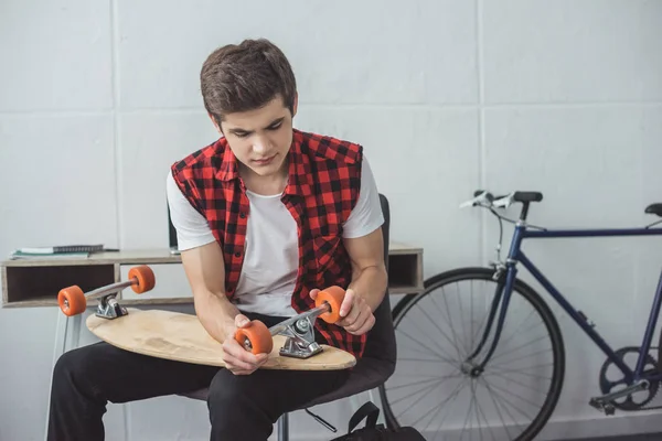 Young skateboarder repairing his longboard at home — Stock Photo