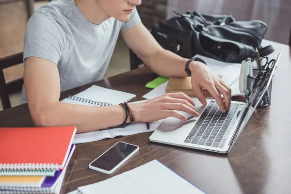 Cropped view of male student doing homework with laptop at table with copybooks — Stock Photo