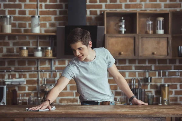 Handsome teenager cleaning table with rag in kitchen — Stock Photo