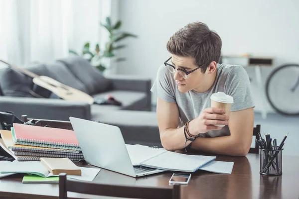 Étudiant mâle avec café faire ses devoirs avec ordinateur portable à la maison — Photo de stock