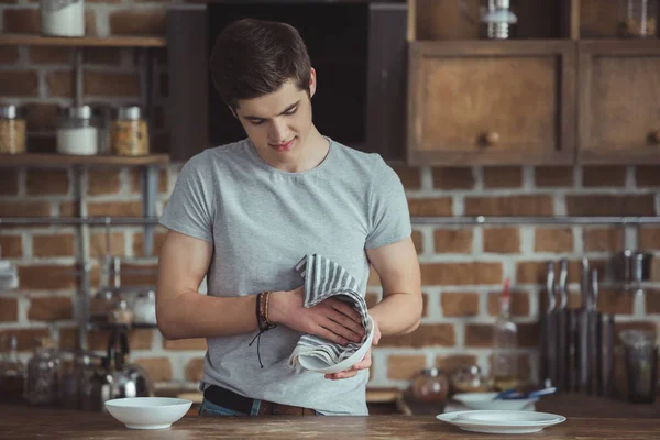 Young male teenager cleaning dinnerware with towel on kitchen — Stock Photo