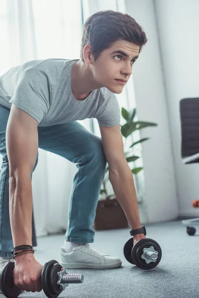 Handsome teenager squatting with dumbbells at home — Stock Photo