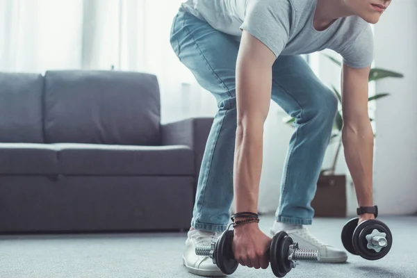 Cropped view of teen boy squatting with dumbbells at home — Stock Photo