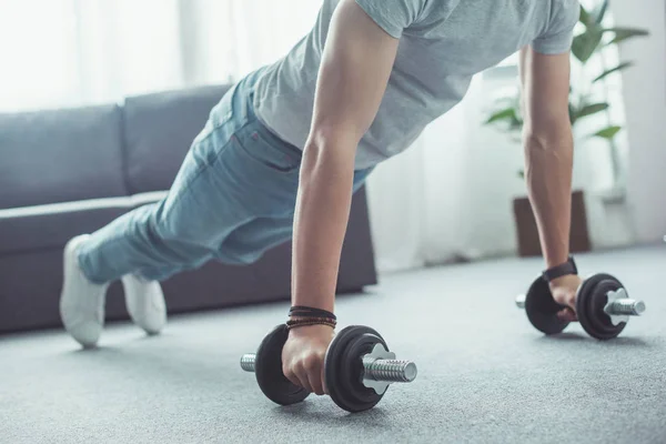 Partial view of young man doing push ups with dumbbells at home — Stock Photo
