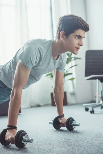 Beau adolescent faire push ups avec haltères à la maison — Photo de stock