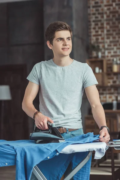 Pensive teen boy ironing blue shirt at home — Stock Photo