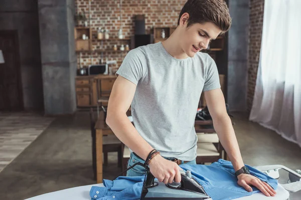 Handsome teenager ironing blue shirt with iron — Stock Photo