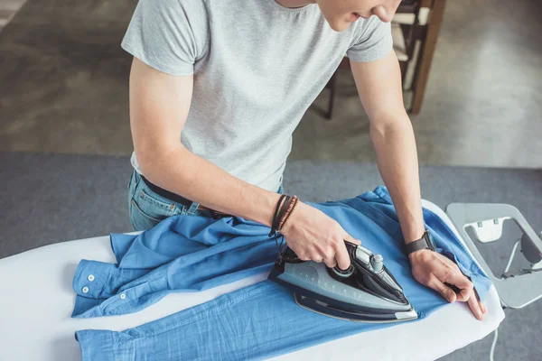 Vista cortada de adolescente engomar camisa azul com ferro em casa — Fotografia de Stock
