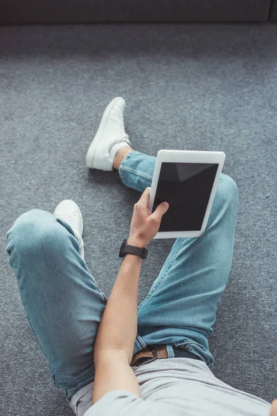 Vista recortada de hombre joven usando tableta con pantalla en blanco mientras está sentado en el suelo - foto de stock