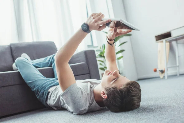 Guapo adolescente chico usando digital tablet mientras está acostado en el suelo - foto de stock