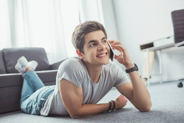 Мужчина улыбающийся подросток разговаривает на смартфоне, лежа на полу — стоковое фото