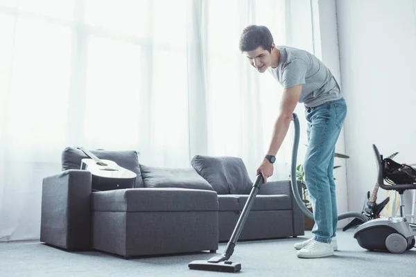 Piso de aspiración adolescente en la sala de estar con aspiradora - foto de stock