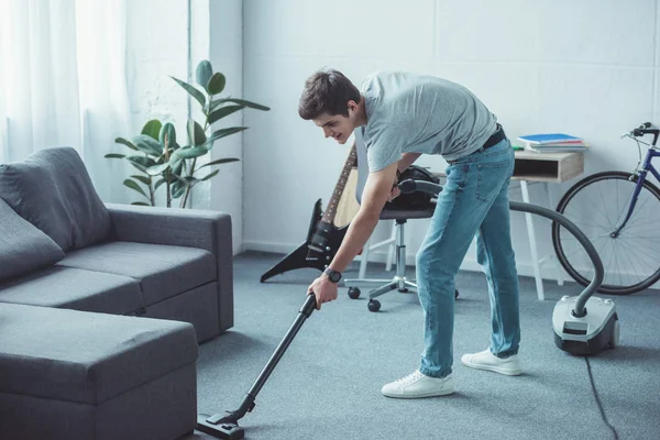 Homme adolescent nettoyage sol près canapé avec aspirateur — Photo de stock