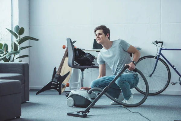 Smiling teenager cleaning floor with vacuum cleaner in living room — Stock Photo