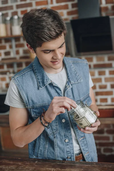 Teen boy putting dollar banknotes into moneybox — Stock Photo