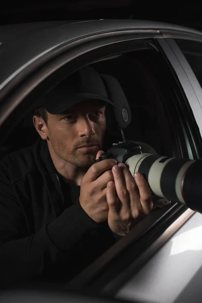 Masculino paparazzi em cap fazendo vigilância por câmera com objeto de vidro de seu carro — Fotografia de Stock