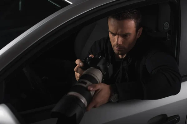 Paparazzi viendo fotografías en cámara con cristal de objeto y haciendo vigilancia desde el coche - foto de stock