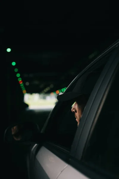 Male paparazzi in cap sitting in car and doing surveillance — Stock Photo