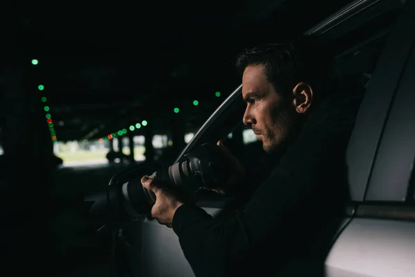 Side view of male paparazzi doing surveillance by camera from his car — Stock Photo