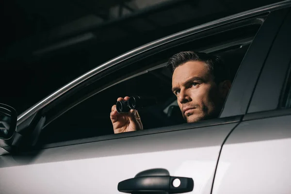 Vista de ángulo bajo de paparazzi macho haciendo vigilancia por binoculares desde el coche - foto de stock