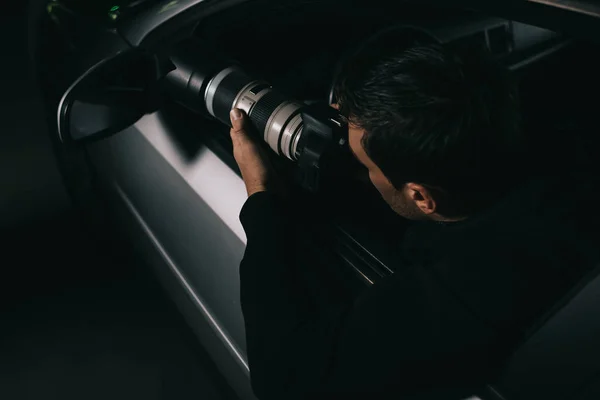 Back view of undercover agent doing surveillance by camera with object glass from his car — Stock Photo