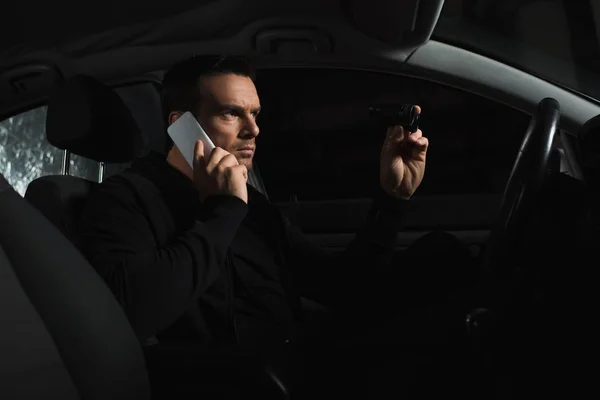 Agente masculino disfarçado concentrado fazendo vigilância por binóculos e falando no smartphone no carro — Fotografia de Stock
