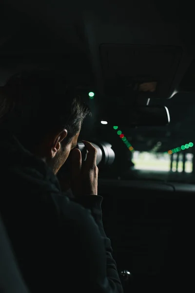 Rear view of man doing surveillance by camera with object glass from his car — Stock Photo