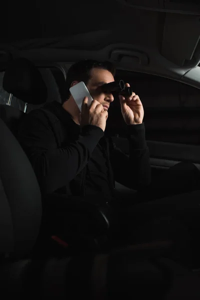Uomo che fa sorveglianza con binocolo e parla su smartphone in auto — Foto stock