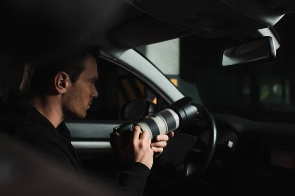 Концентрированный мужчина-папарацци делает наблюдения с помощью камеры с объективом из своей машины — стоковое фото