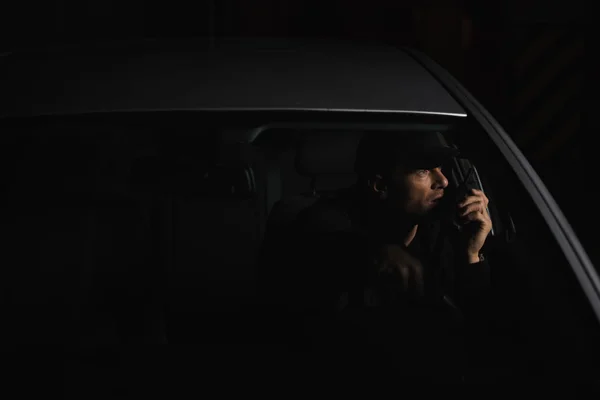 Vue de face de détective privé masculin en casquette en utilisant talkie walkie dans la voiture — Photo de stock