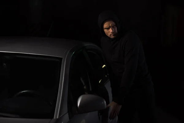 Focused male thief in black hoodie intruding automobile — Stock Photo