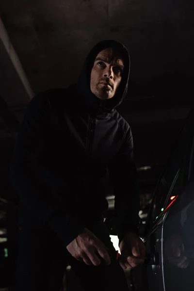 Cautious male robber in black hoodie intruding car by screwdriver — Stock Photo