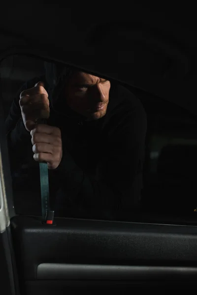 Cautious male thief in black hoodie intruding car by crowbar — Stock Photo