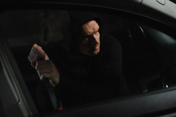 Серйозний чоловічий грабіжник у чорному светрі, що залучає машину на кермі — стокове фото