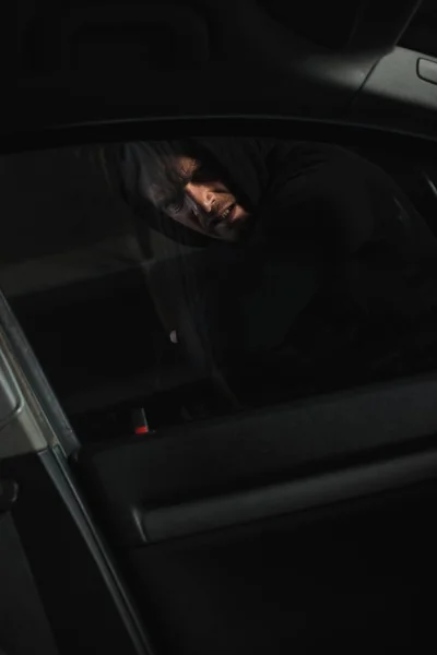 Concentrated male robber breaking car window by elbow — Stock Photo
