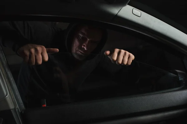 Focused male robber in black hoodie intruding car — Stock Photo