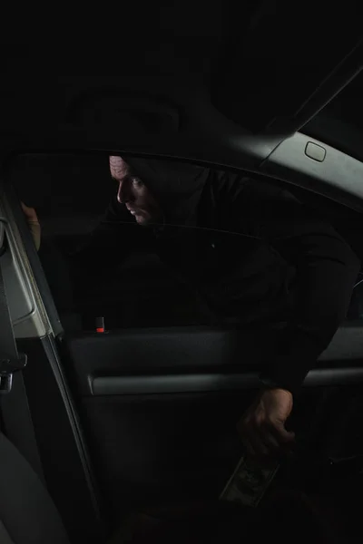 Обережний чоловічий грабіжник у чорному светрі краде доларові банкноти з автомобіля — стокове фото