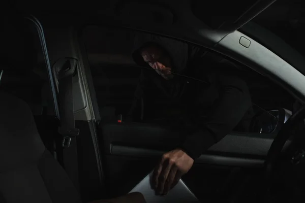 Ladro maschio con cappuccio nero rubare laptop da auto — Foto stock