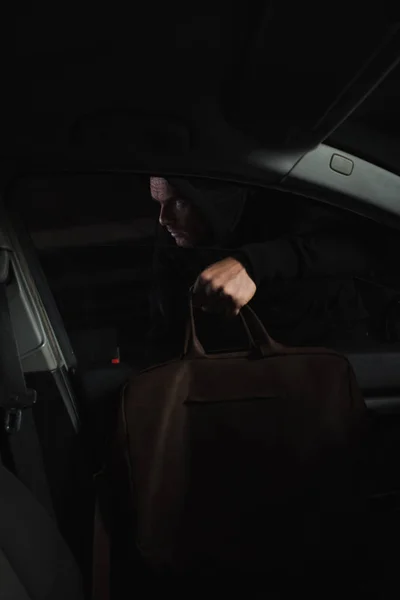 Cautious male thief in black hoodie stealing bag from car — Stock Photo