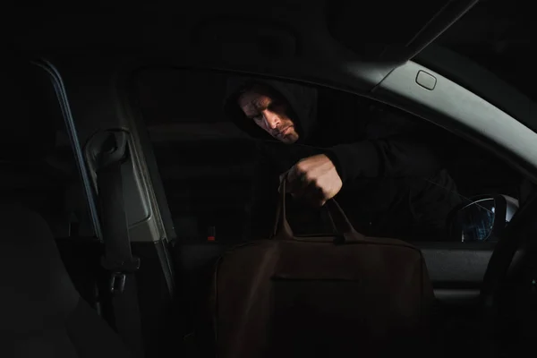 Männlicher Räuber in schwarzem Kapuzenpullover stiehlt Tasche aus Auto — Stockfoto
