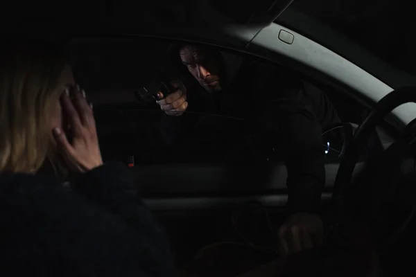 Вор мужчина, стреляющий из пистолета и крадущий сумку у женщины, сидящей в машине — стоковое фото
