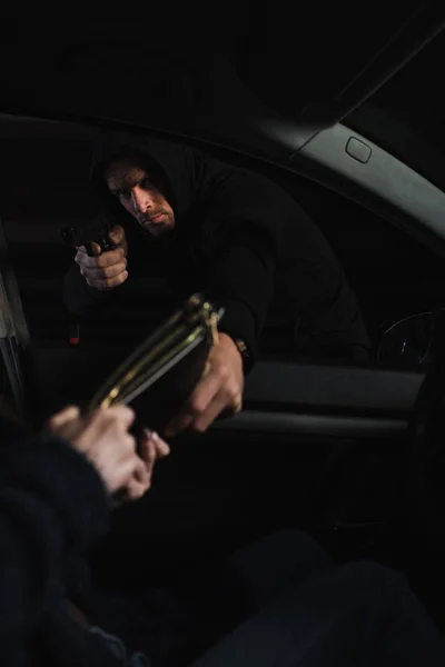 Серьезный вор мужчина прицеливается пистолетом и крадет сумку у женщины, сидящей в машине — стоковое фото