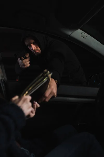 Serious male thief aiming by gun and stealing bag from woman sitting in car — Stock Photo