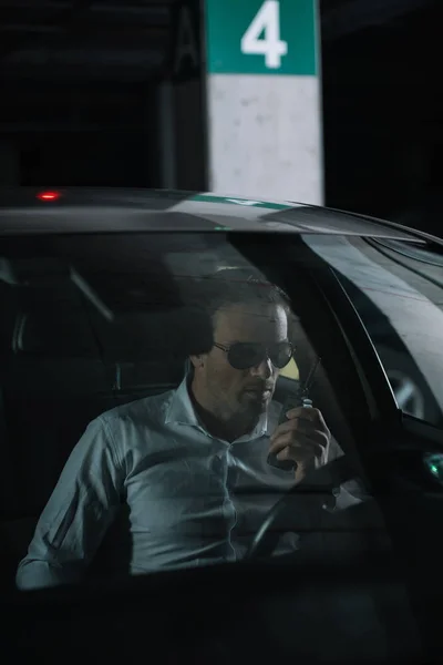 Male undercover agent in sunglasses doing surveillance and using talkie walkie in car — Stock Photo