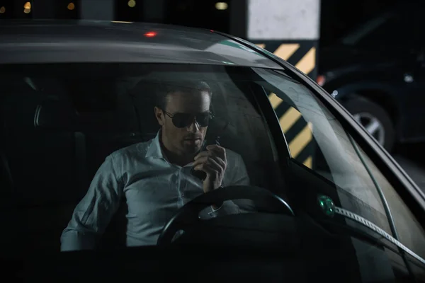 Male undercover agent in sunglasses using talkie walkie and sitting in car — Stock Photo